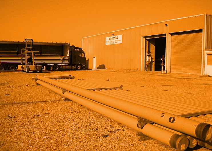 Alphapipe : Spécialiste Tubes Acier et Logistique Industrielle Tubes en acier stockés devant l'entrepôt Alphapipe avec un camion et un chariot élévateur en arrière-plan.